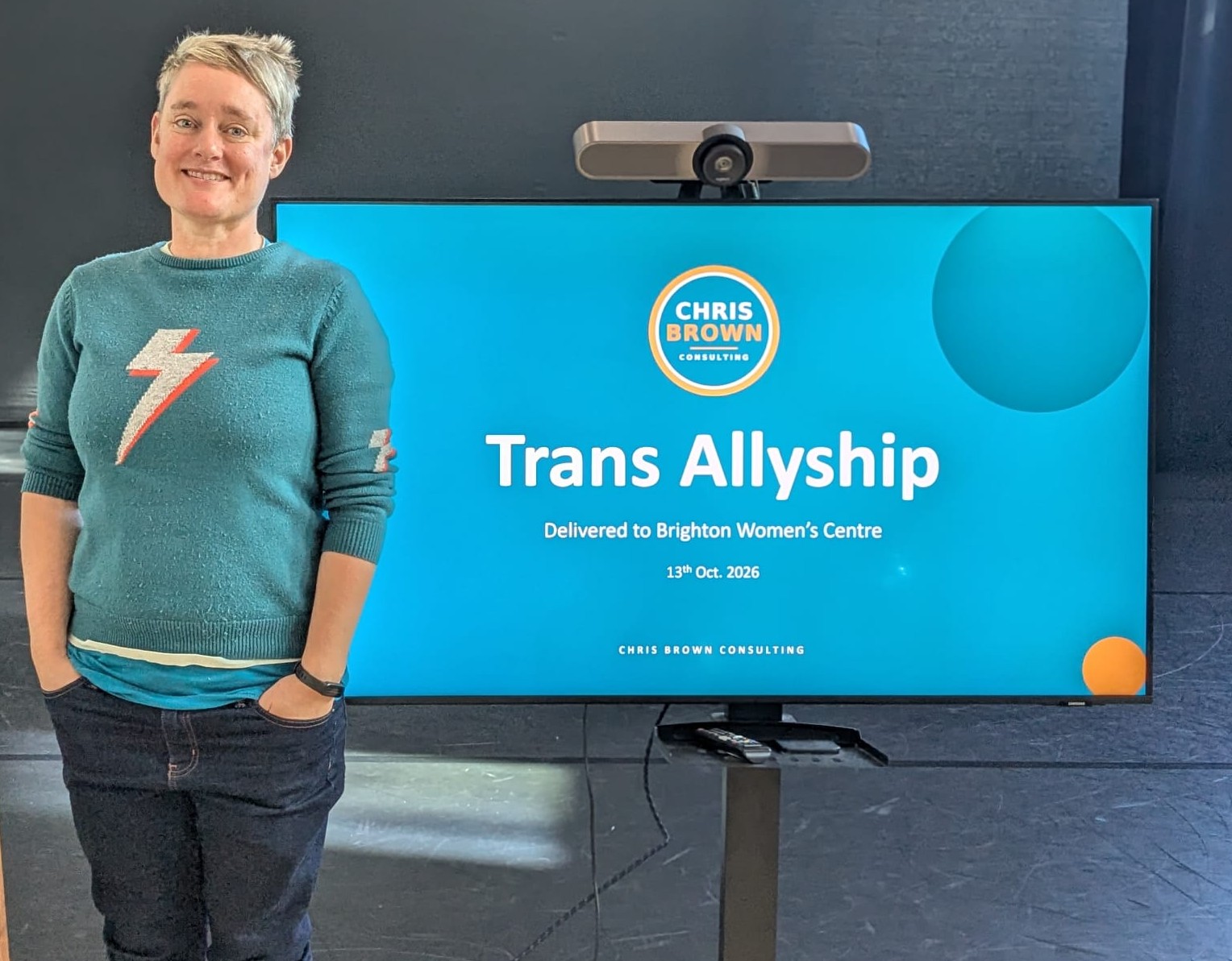Chris Brown standing beside a screen showing the title slide: Trans Allyship, delivered to Brighton Women’s Centre